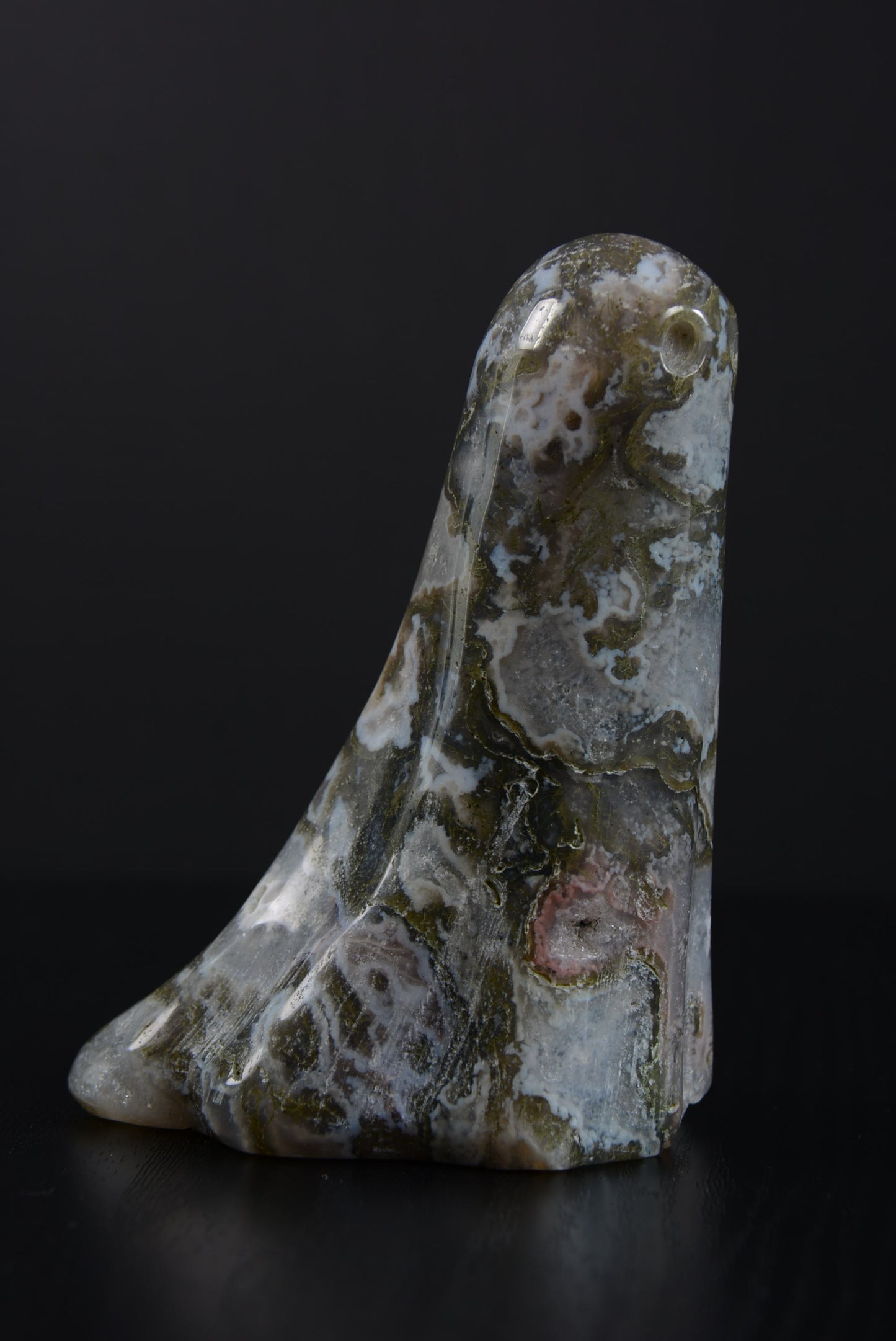 Side view of a polished ghost ornament, revealing the meticulous detail of its carving, with the natural gemstone's unique patterns and hues elegantly displayed, embodying a timeless spirit.